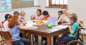 Young teacher helping a child in a wheelchair doing homework.