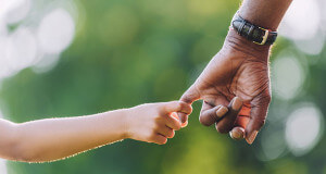 Adult hand wearing watch holding a child's hand outdoors.