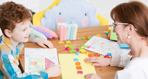 Teacher and student sitting at a desk doing creative activities.