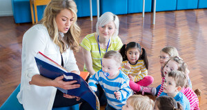 Two female preschool teachers reading to seven children.